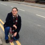 Cllr Zoë Kirk-Robinson kneeling on Park Road, with the double-yellow lines that are due to be removed.